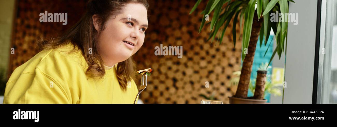 Una giovane donna sicura di sé con la sindrome di Down siede in un bar, assaporando il suo pasto e sorridendo calorosamente. Foto Stock