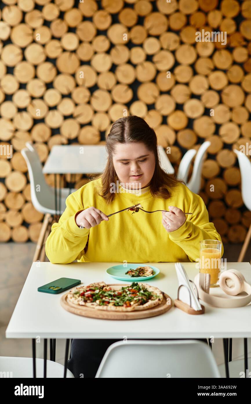 Una giovane donna con sindrome di Down si diverte a mangiare in un caffè informale, mostrando sicurezza e stile. Foto Stock
