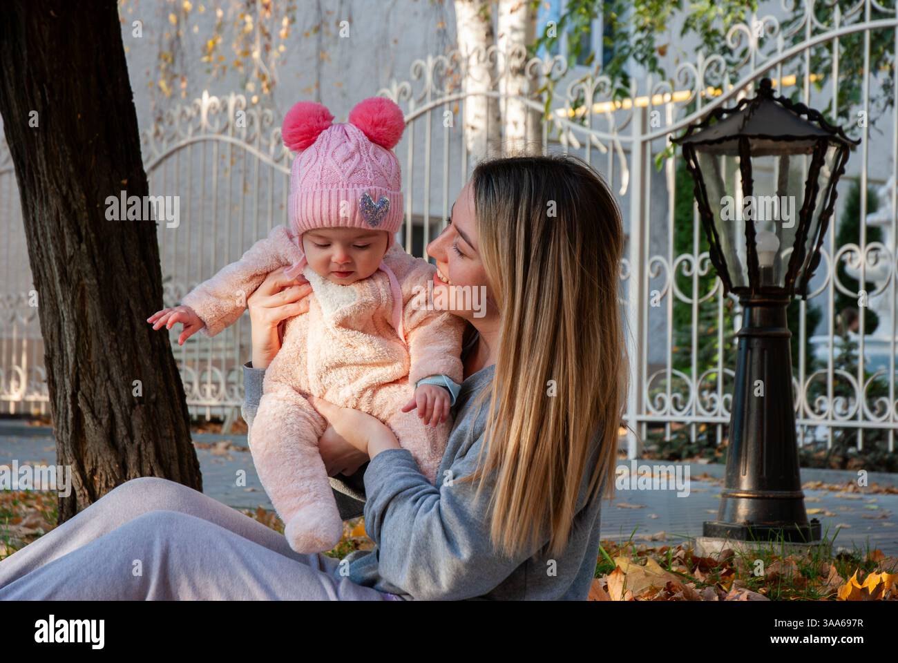 Mamma e bambino in caldi abiti autunnali che giocano all'aperto in un parco alberato. Foto Stock