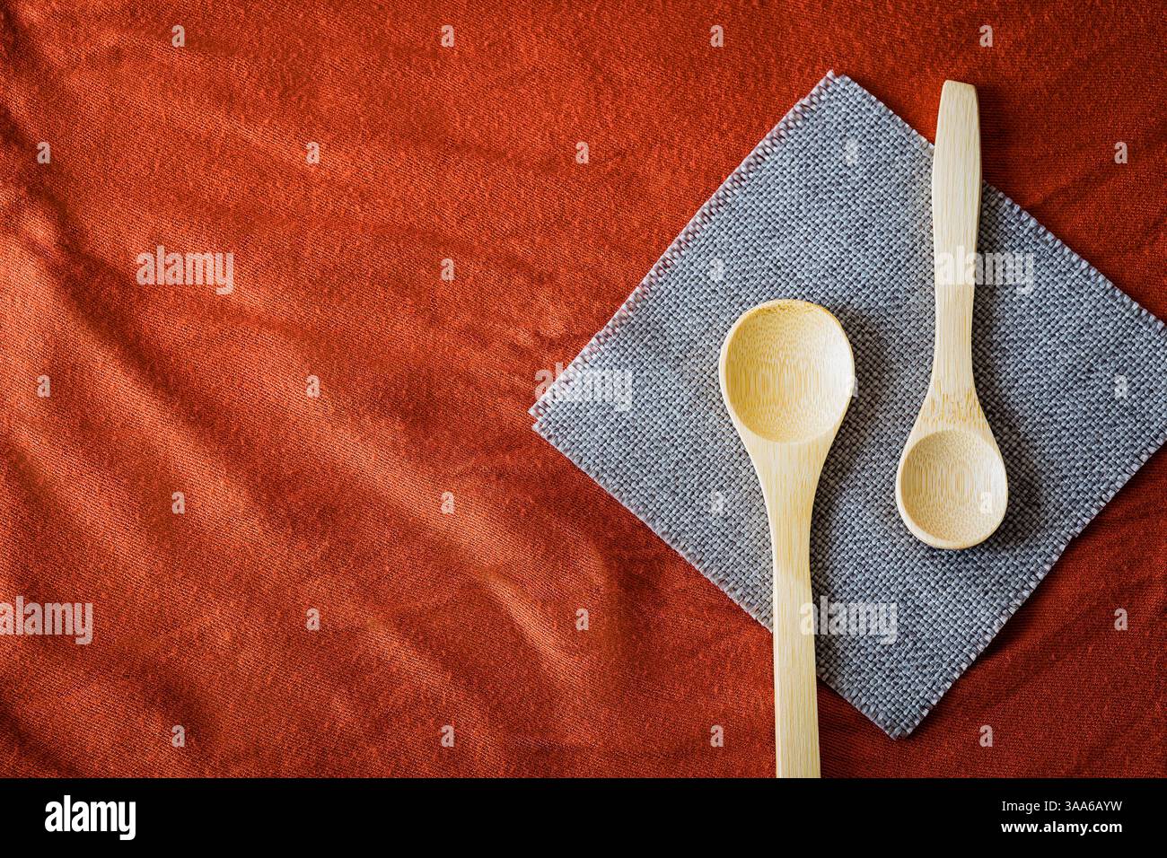 Cucchiai di legno su un tovagliolo grigio su fondo in tessuto rosso testurizzato. Utensili da cucina rustici ed eco-compatibili con tonalità calde e naturali e una Foto Stock