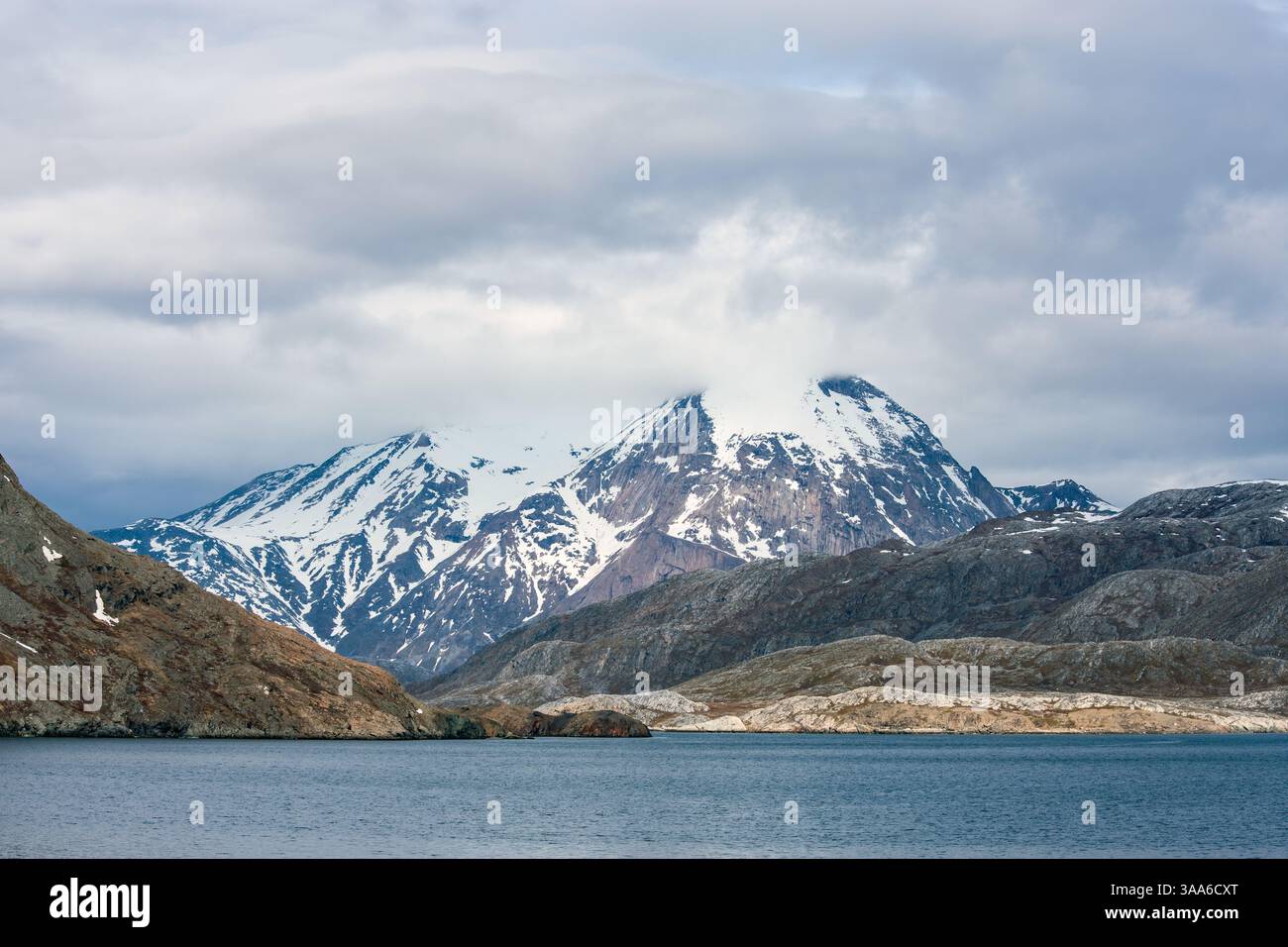 Montagne innevate che torreggiano sulle acque scure del fiordo di Arsuk, in Groenlandia, con un cielo blu vibrante che crea un contrasto sorprendente nell'Artico. Foto Stock