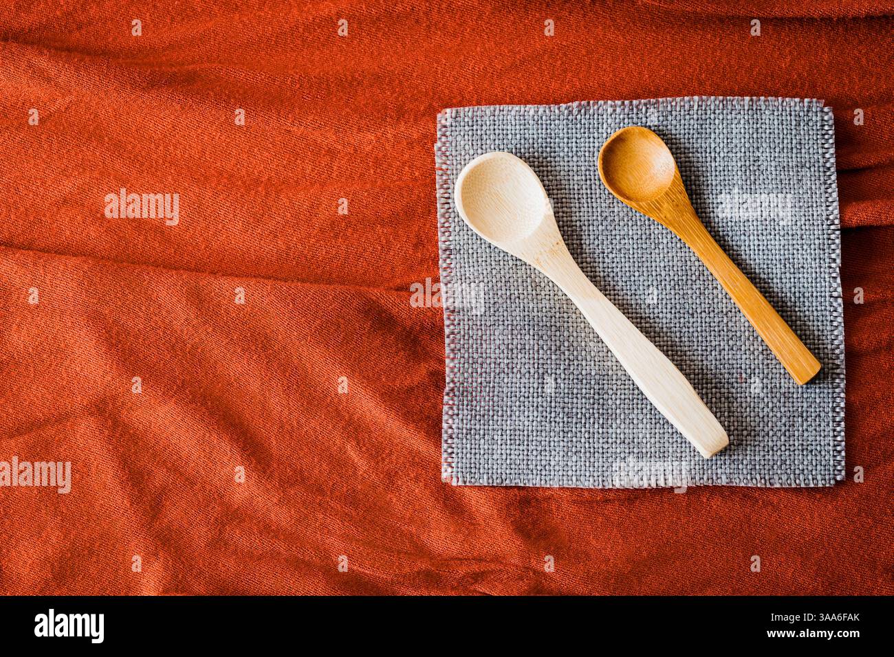 Cucchiai di legno su un tovagliolo grigio su fondo in tessuto rosso testurizzato. Utensili da cucina rustici ed eco-compatibili con tonalità calde e naturali e una Foto Stock