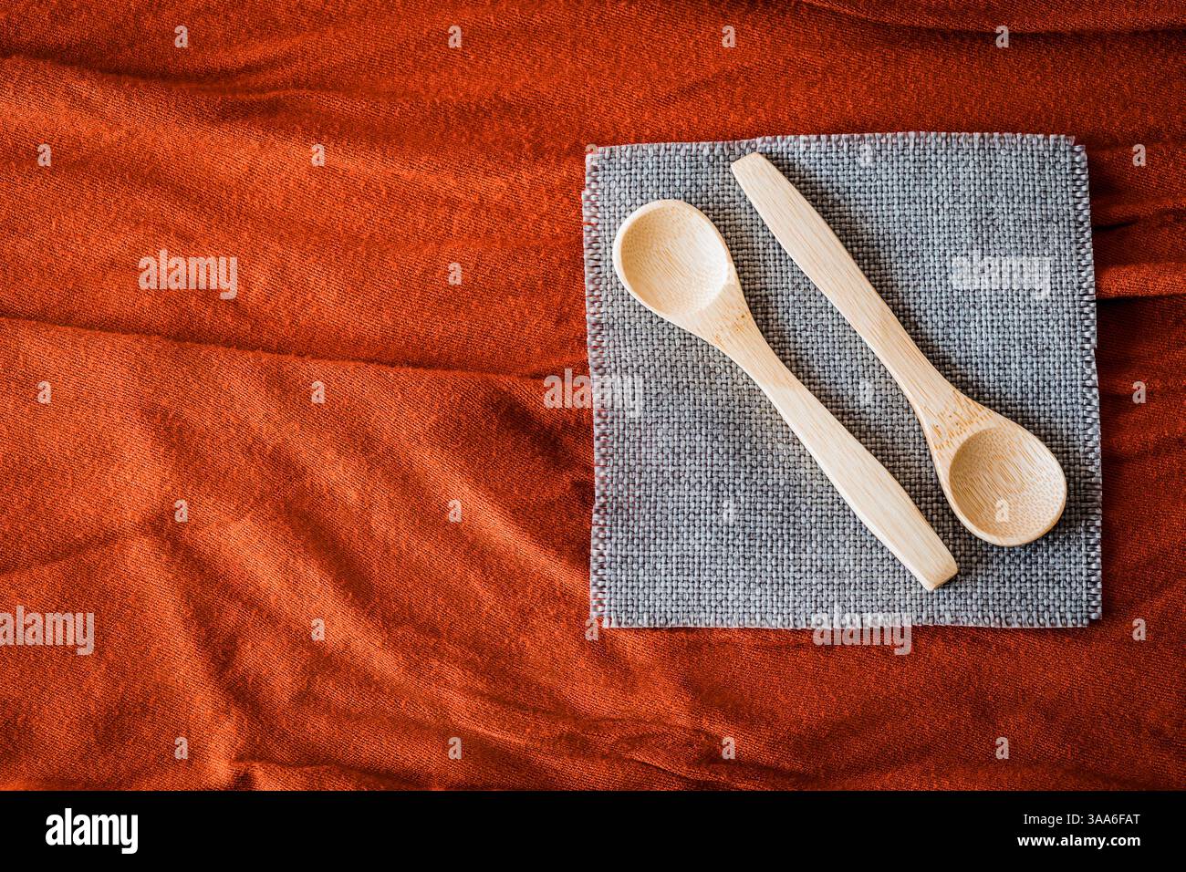 Cucchiai di legno su un tovagliolo grigio su fondo in tessuto rosso testurizzato. Utensili da cucina rustici ed eco-compatibili con tonalità calde e naturali e una Foto Stock