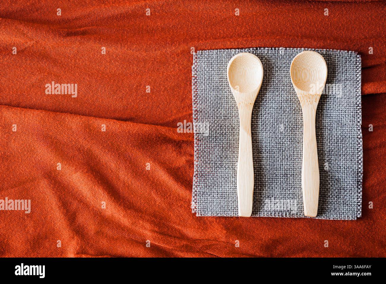 Cucchiai di legno su un tovagliolo grigio su fondo in tessuto rosso testurizzato. Utensili da cucina rustici ed eco-compatibili con tonalità calde e naturali e una Foto Stock