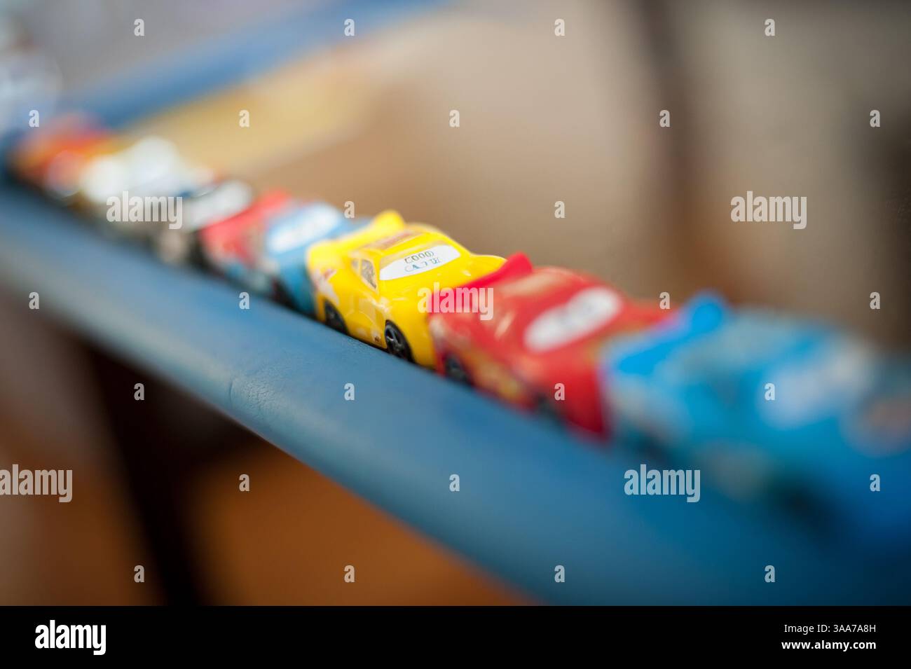 Le macchinine colorate sono disposte in linea retta su un tavolo blu, invitando il gioco e l'immaginazione in un caldo ambiente interno. Il loro vibrante d Foto Stock