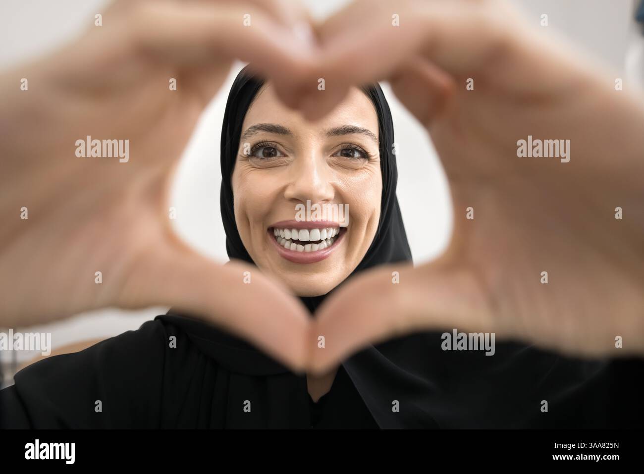 Donna araba sorridente attraverso una cornice a forma di cuore realizzata con le mani Foto Stock