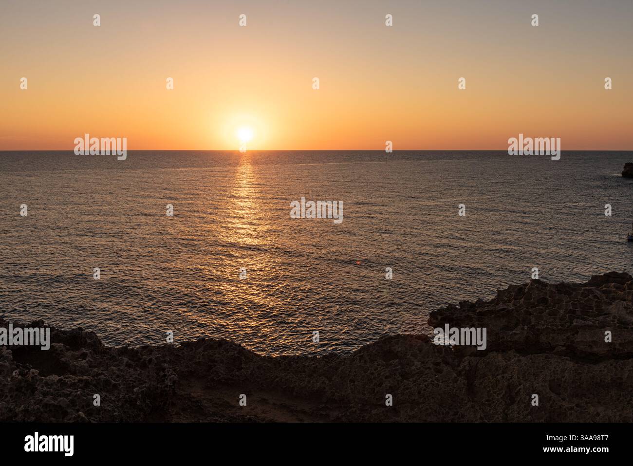 Il mare sereno all'alba o al tramonto, con acque tranquille e tranquille. Cielo arancione, cielo limpido, acque calme, rocce, spazio vuoto, Mar Mediterraneo. Foto Stock
