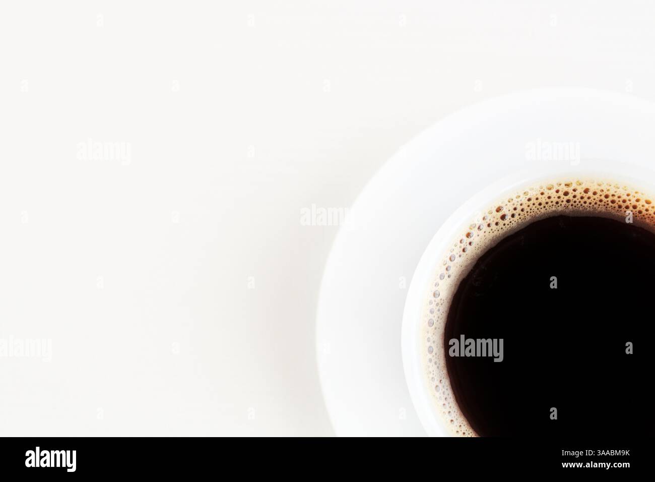 Vista dall'alto del caffè nero in una tazza bianca posizionata nell'angolo inferiore su una superficie bianca. Stile minimalista, luminoso e moderno. Foto Stock