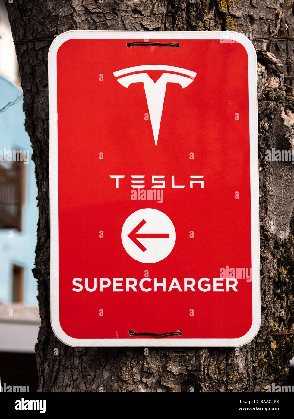 Innsbruck, Austria - 21 marzo 2025: Un cartello rosso con il logo Tesla e la parola SUPERCHARGER con una freccia rivolta verso sinistra, montato su un albero. Foto Stock