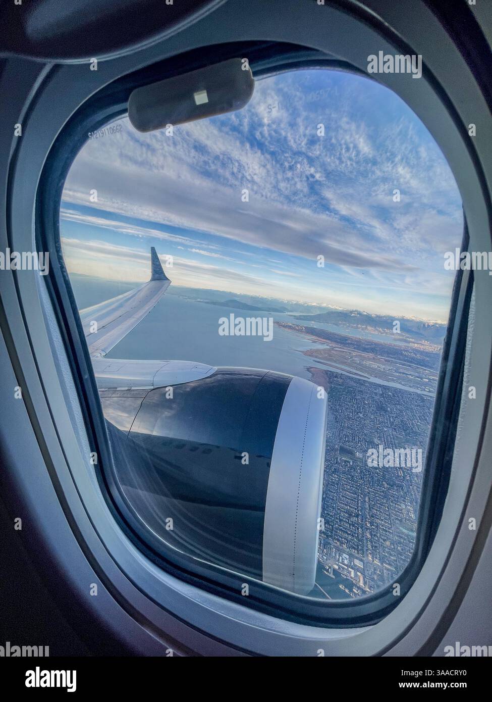 Vista dall'interno di un aereo, guardando fuori dalla finestra l'ala e il motore su un paesaggio costiero. Foto Stock