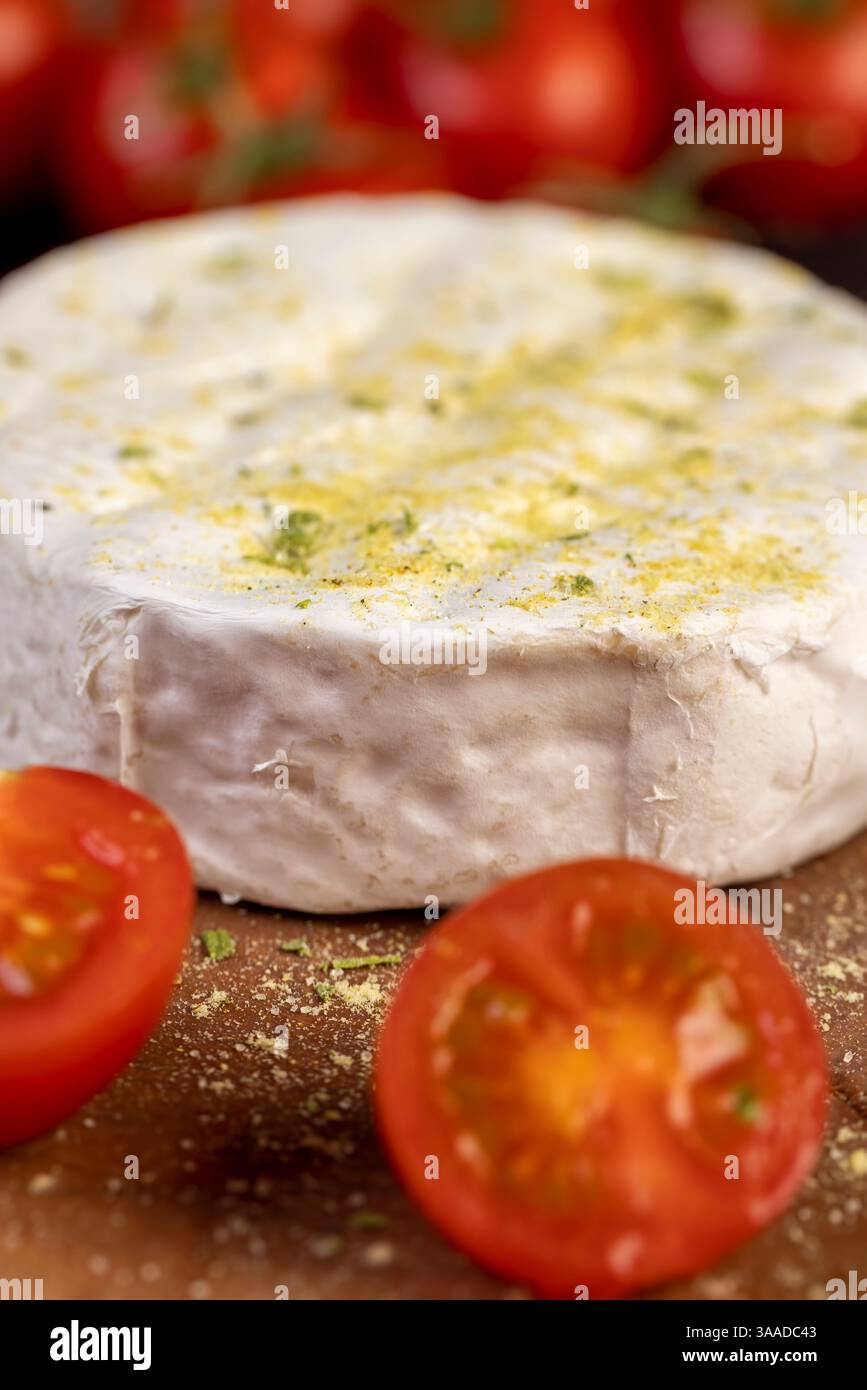 formaggio morbido con muffa cosparsa di spezie e piccoli pomodori rossi maturi, formaggio morbido bianco con sale e spezie e pomodori rotondi rossi piccoli sul tabl Foto Stock