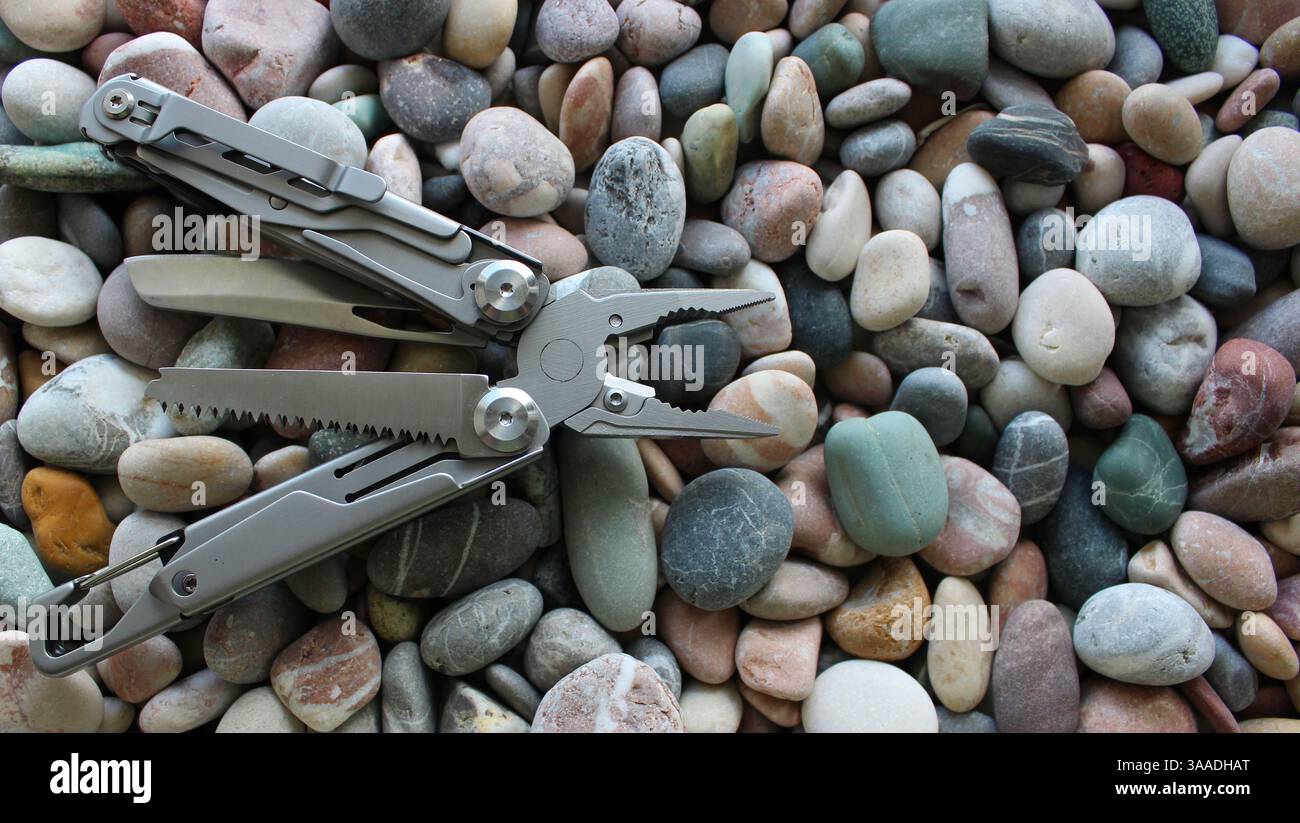 Foto di scorta di attrezzature per esterni. Strumento multifunzione in metallo con strumenti piegati su pietre marine a lato dell'immagine Foto Stock