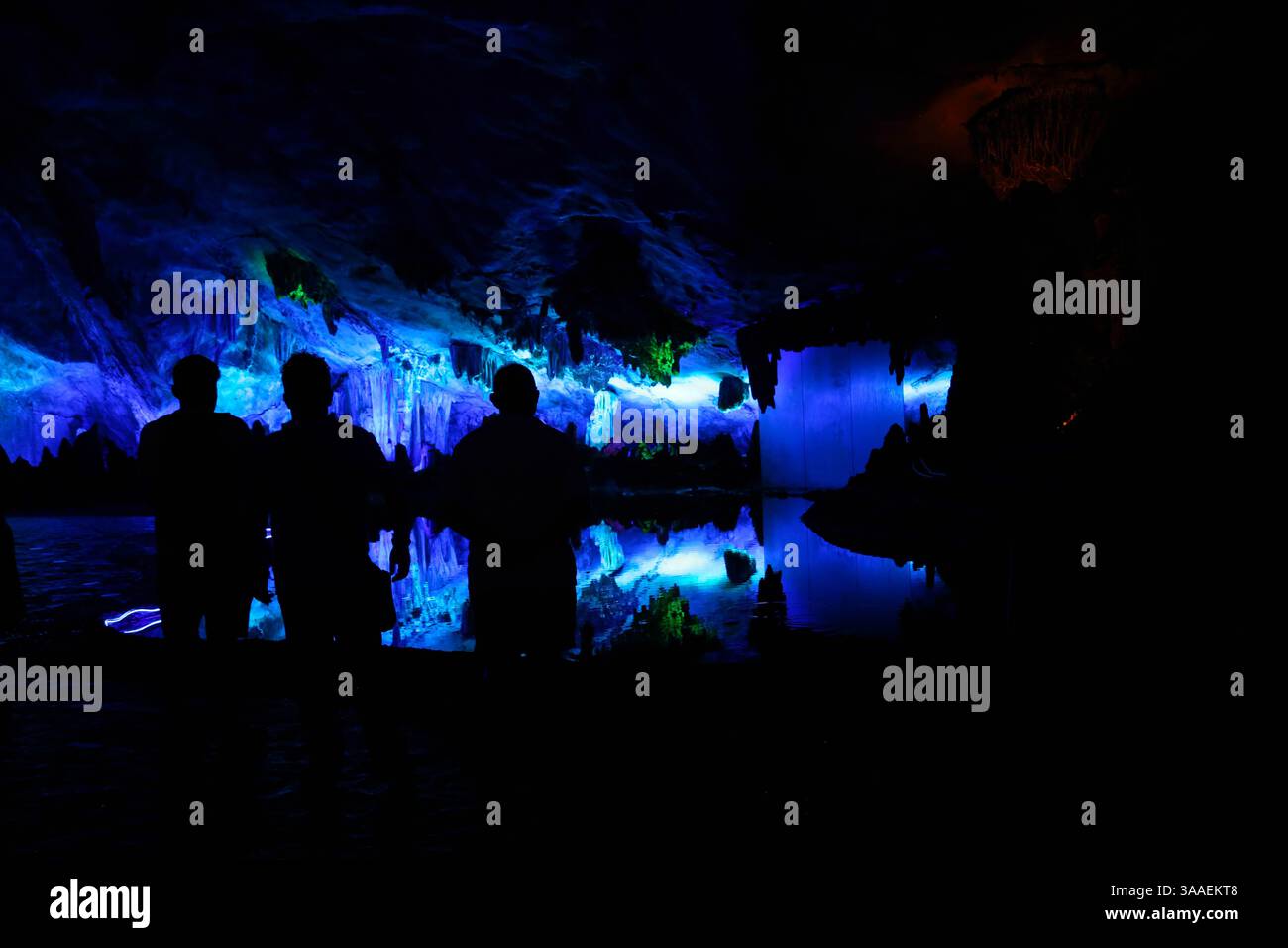 Figure sagomate contro il muro a luce blu e la riflessione nella grotta del flauto di canna (Guilin, Cina) - 7 settembre 2024 Foto Stock