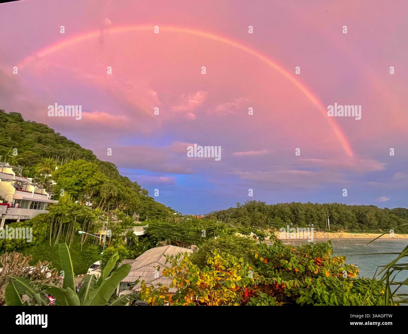 Arcobaleno sopra una spiaggia tropicale Un arcobaleno mozzafiato sopra una spiaggia tropicale al tramonto. Il cielo pastello si riflette sulle calme acque dell'oceano Foto Stock
