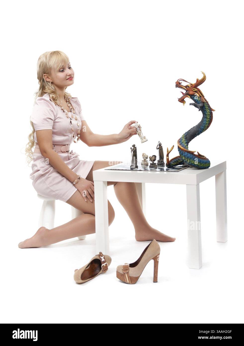 Bella ragazza bionda che gioca a scacchi con un drago decorativo. Isolare su bianco Foto Stock
