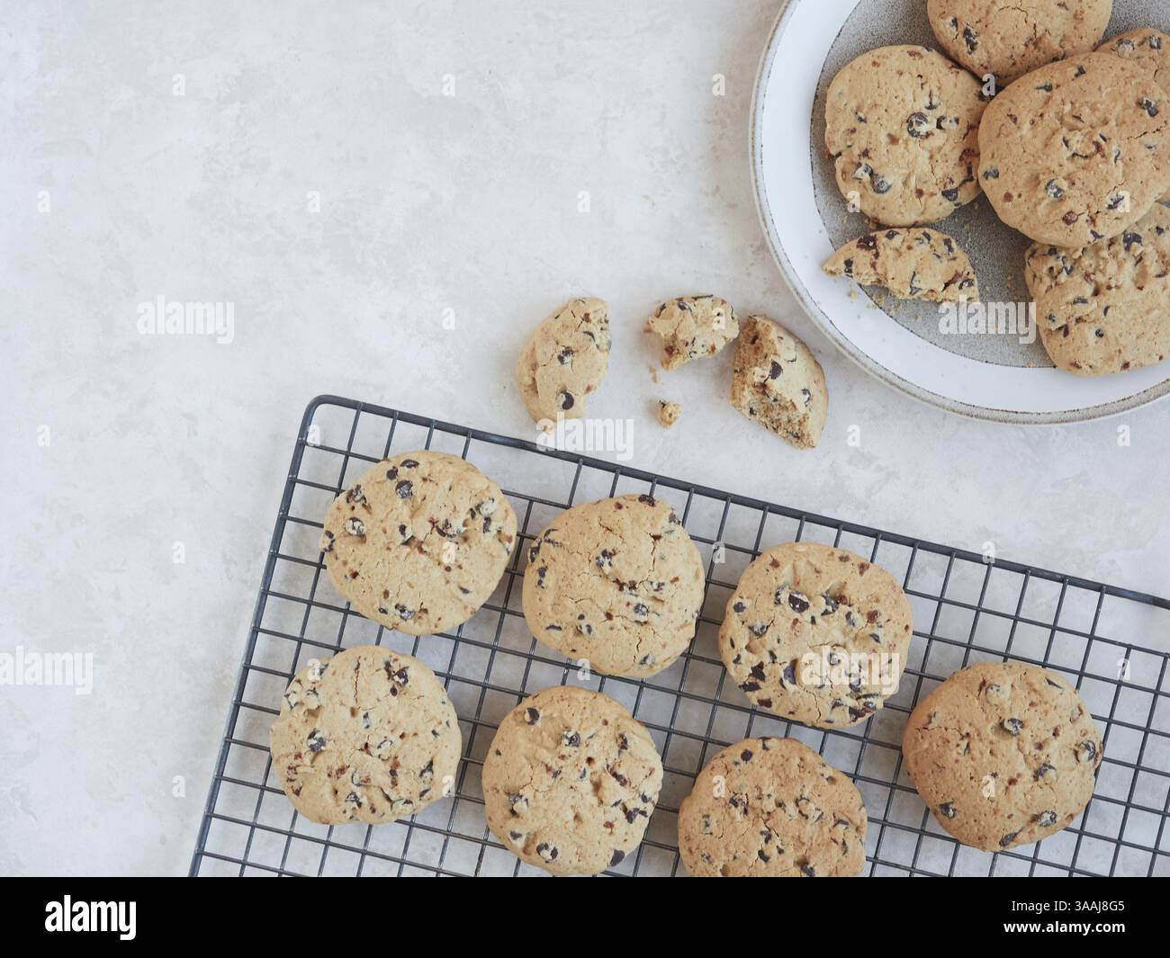 Biscotti fatti in casa con gocce di cioccolato appena sfornati su una griglia rinfrescante, serviti in un piatto e un pezzo sbriciolato sul piano di lavoro. Vista dall'alto, copia spazio Foto Stock