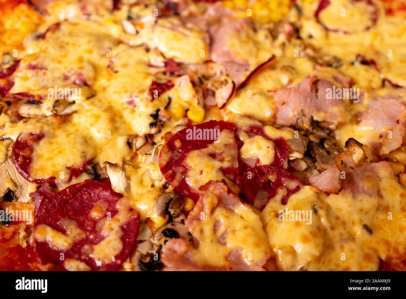 Una pizza fresca è ricoperta di formaggio fuso, fette di prosciutto e peperoni. La crosta è marrone dorato e i condimenti includono funghi e mais. Perfe Foto Stock
