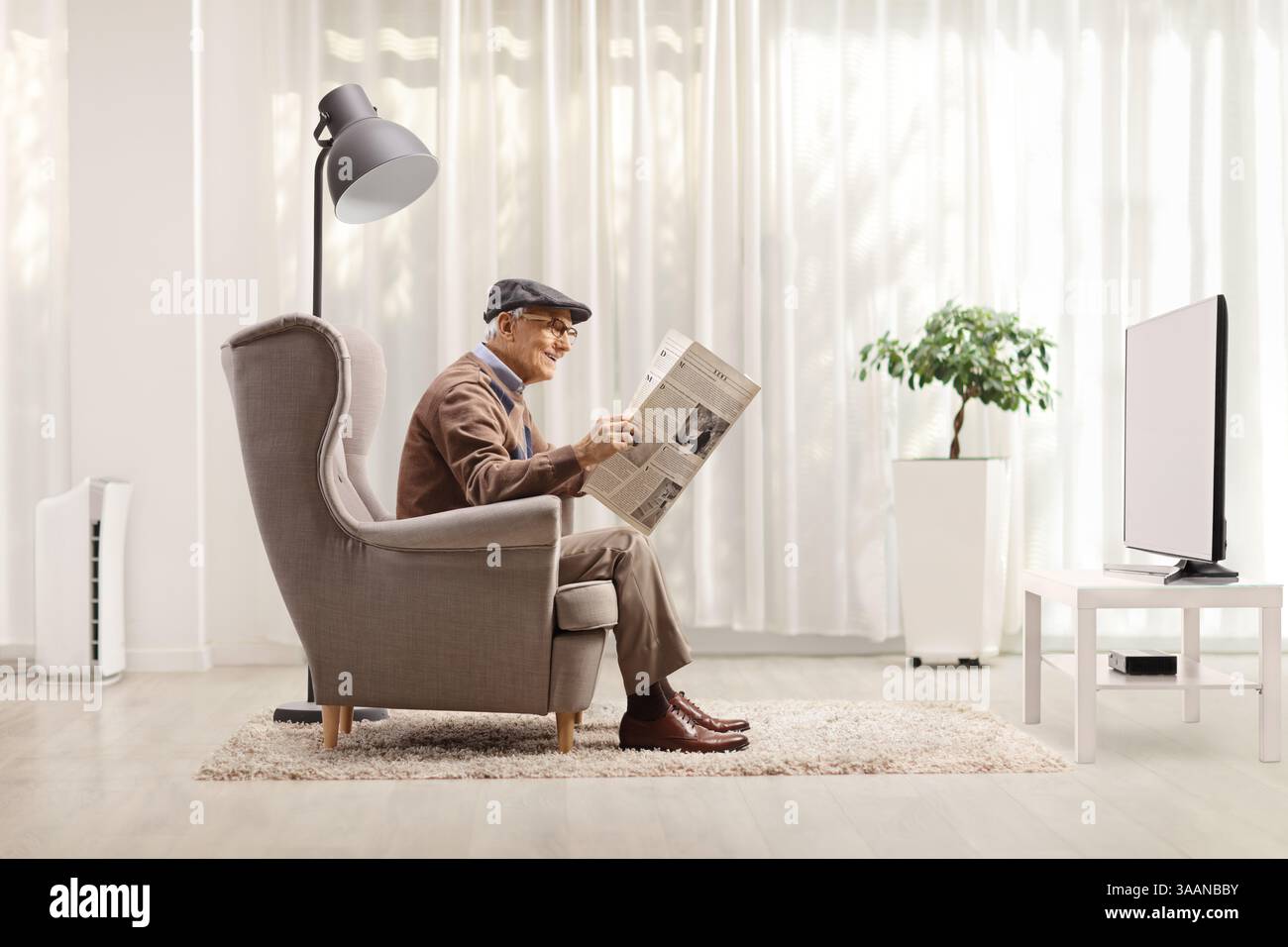 Uomo anziano in poltrona che legge un giornale davanti alla tv Foto Stock