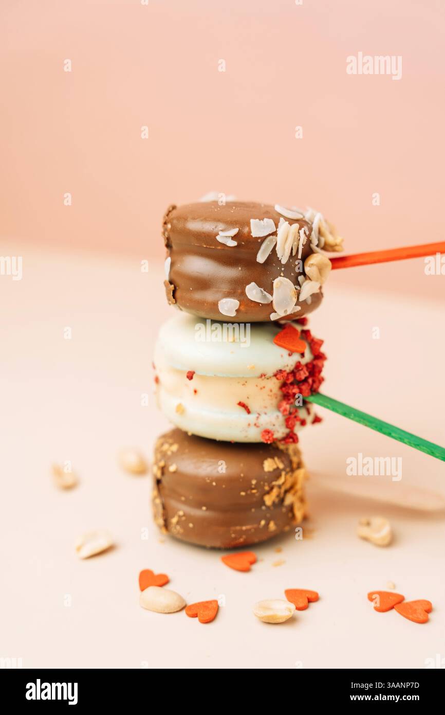 Dessert francesi al cioccolato. Macaron per torte su sfondo rosa, colori pastello, macaroon decorato con noci e cuori diversi, foto verticale. Foto Stock