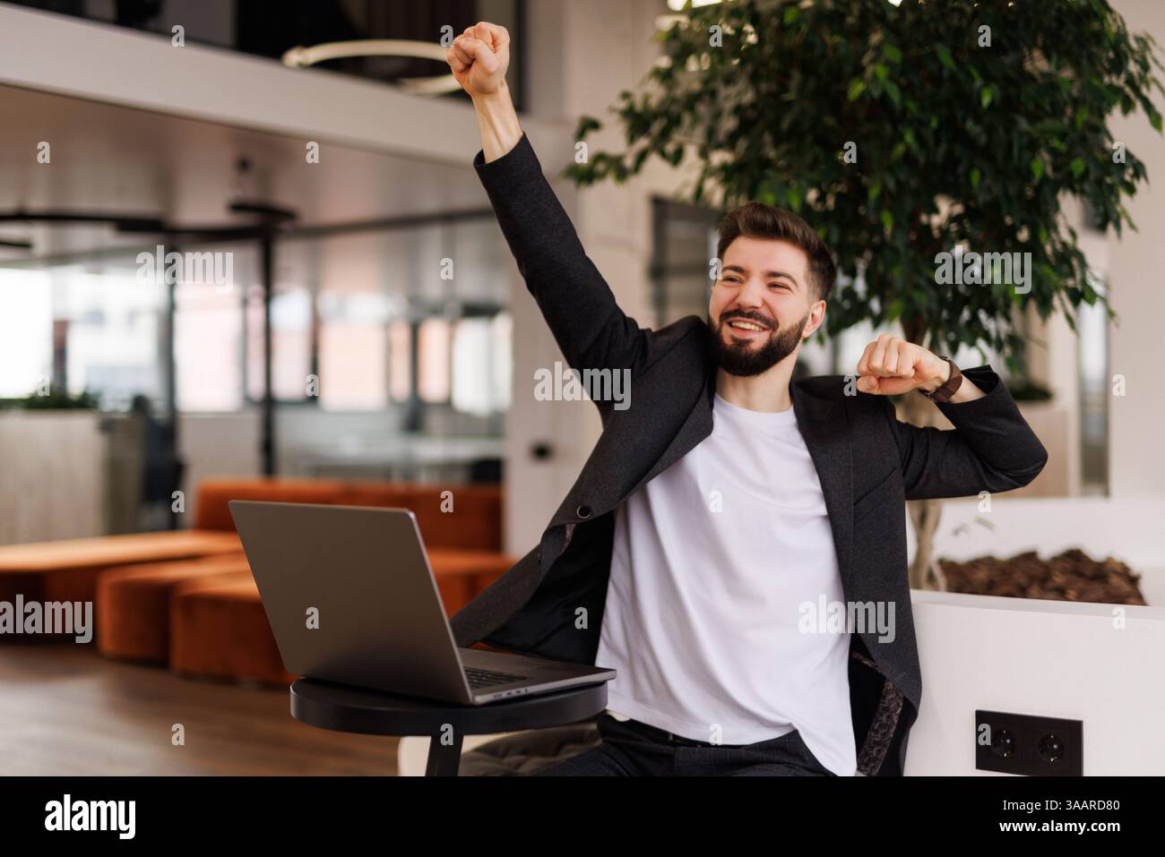 Eccitato gridare giovane uomo guardando lo schermo del suo computer e trionfare con le mani sollevate Foto Stock
