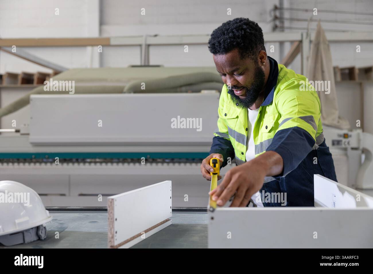 Lavoratore del personale africano nero che lavora utilizzando il metro a nastro compensato prodotto di mobili in legno in fabbrica con tuta di sicurezza Foto Stock Lavoratore del personale africano nero che lavora utilizzando il metro a nastro compensato prodotto di mobili in legno in fabbrica con tuta di sicurezza Foto Stock