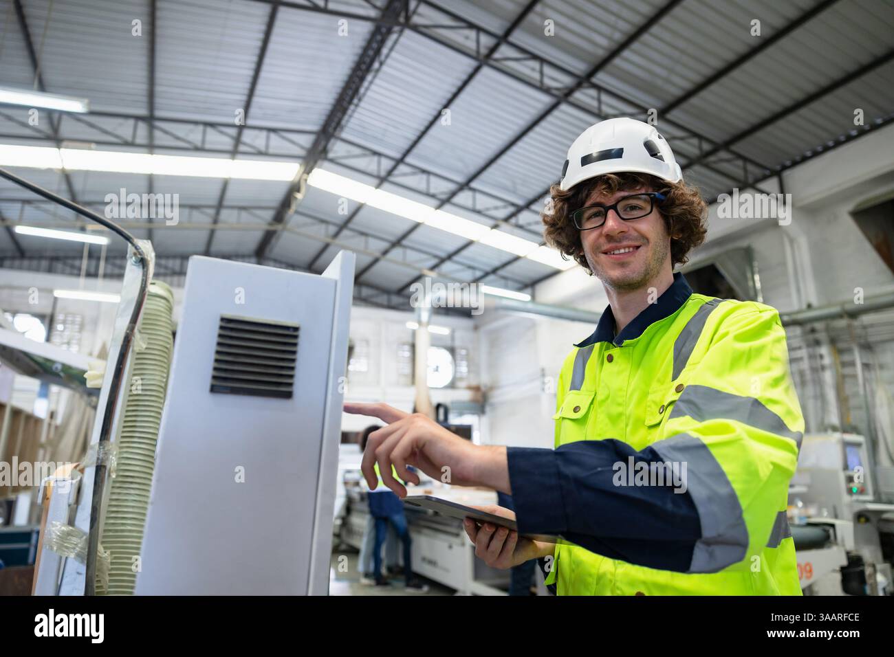 Ritratto giovane Caucasico maschio controllo lavoratore operare macchina CNC taglierina per legno nell'industria di fabbrica di mobili con tuta di sicurezza Foto Stock