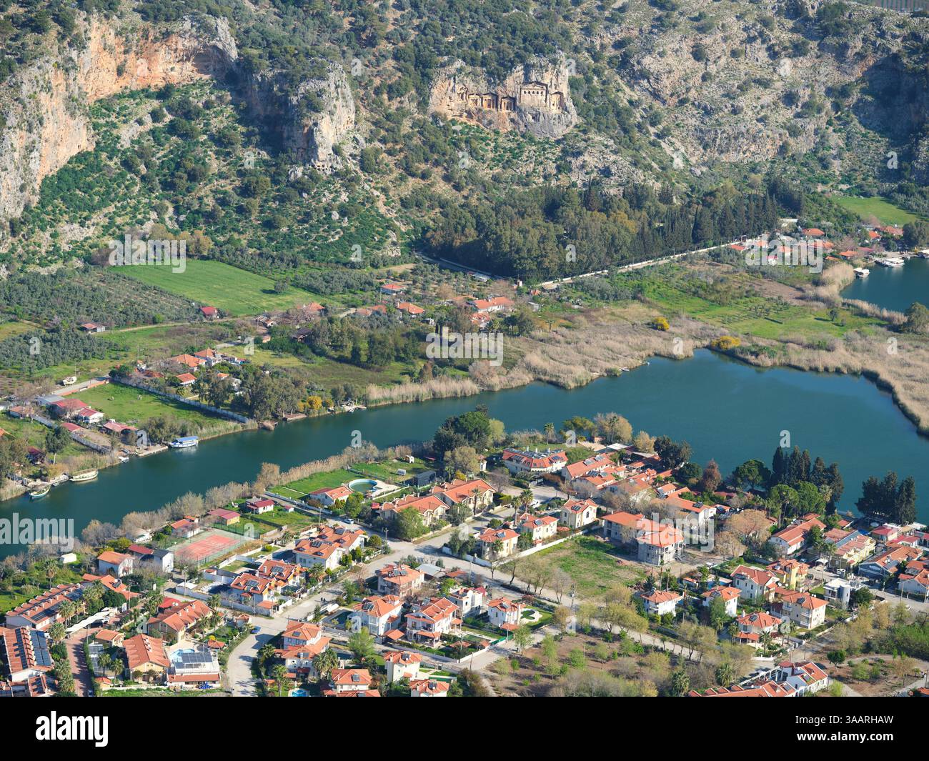 VISTA AEREA. Città di Dalyan sulla riva sinistra del fiume Dalyan e dall'altra parte del fiume le tombe scavate nella roccia di Kaunos. Dalyan, provincia di Muğla, Turchia. Foto Stock