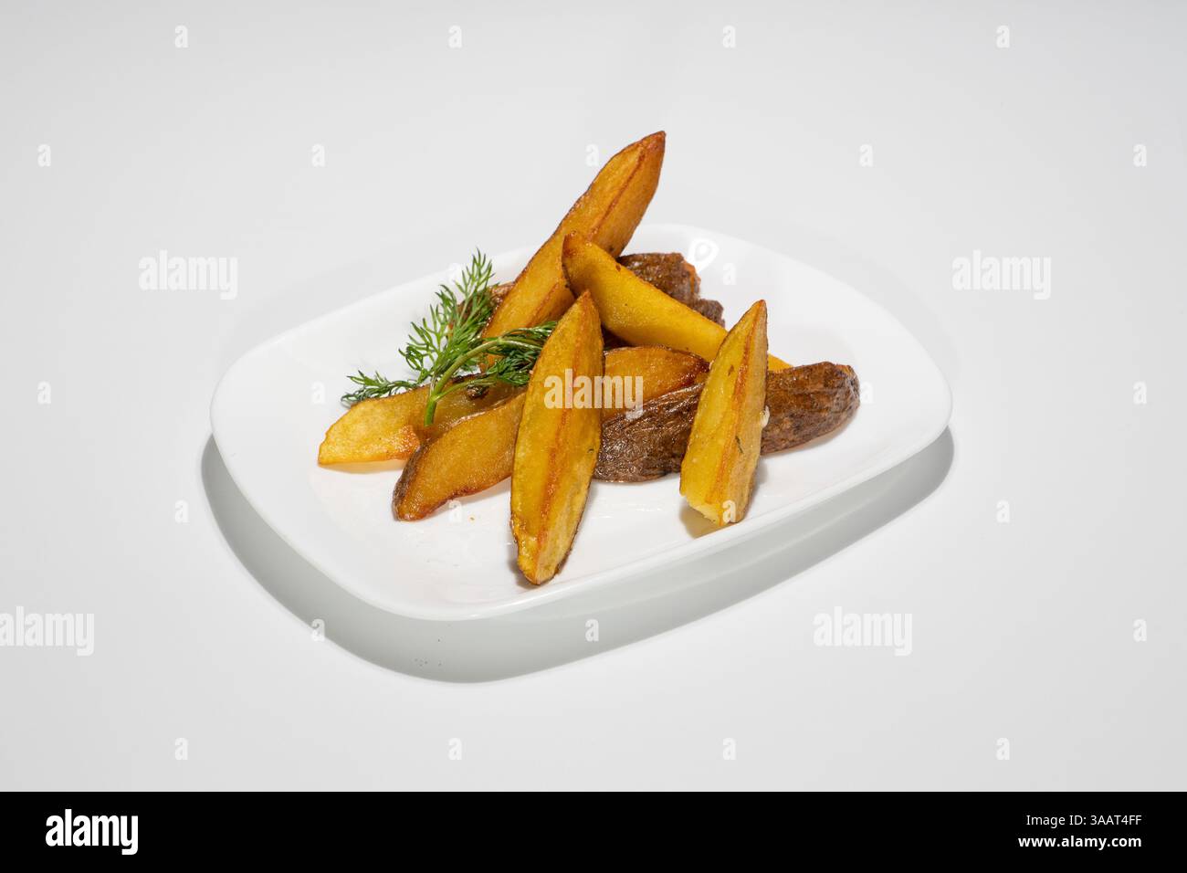 Appetitose patate fritte dorate fritte con erbe verdi fresche sul piatto bianco. Foto Stock