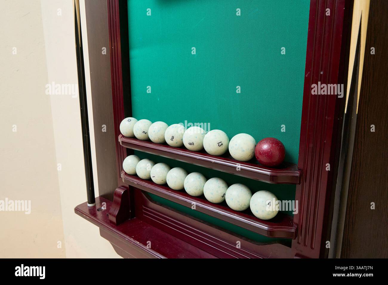 Tabellone segnapunti da biliardo che mostra una collezione di palline bianche numerate e una singola pallina rossa su sfondo verde in feltro, ordinatamente disposte su ripiani in legno Foto Stock
