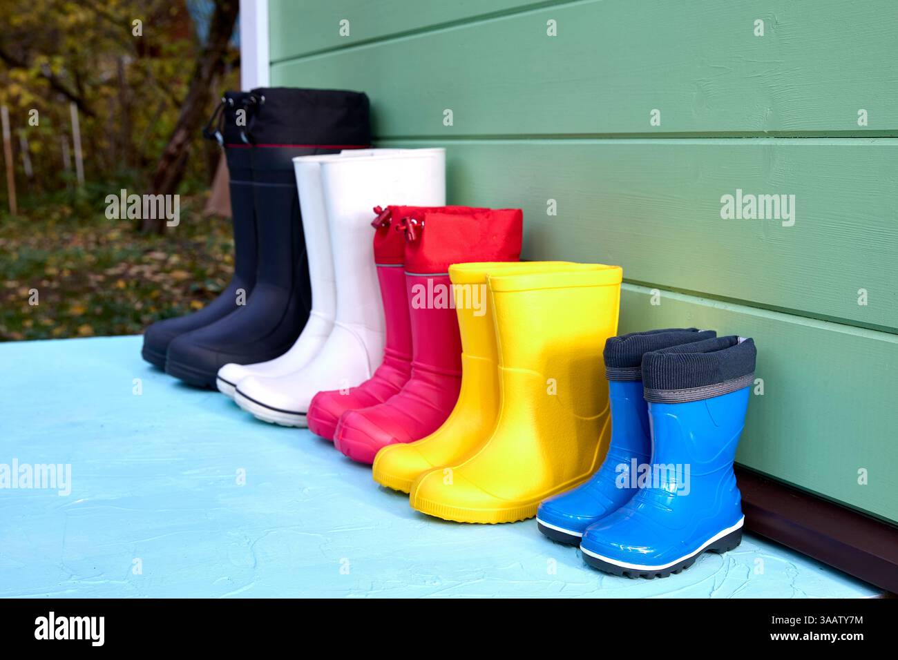 Una fila di stivali in gomma colorati disposti in modo ordinato contro una parete verde. Varie dimensioni e tonalità vivaci suggeriscono la preparazione per le avventure all'aria aperta in qualsiasi WE Foto Stock