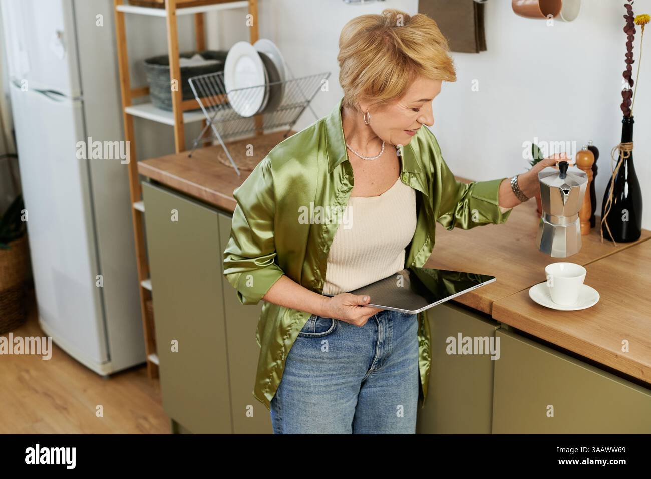 Una donna anziana prepara il caffè con una macchina per caffè espresso nella sua accogliente cucina, sentendosi contenta. Foto Stock