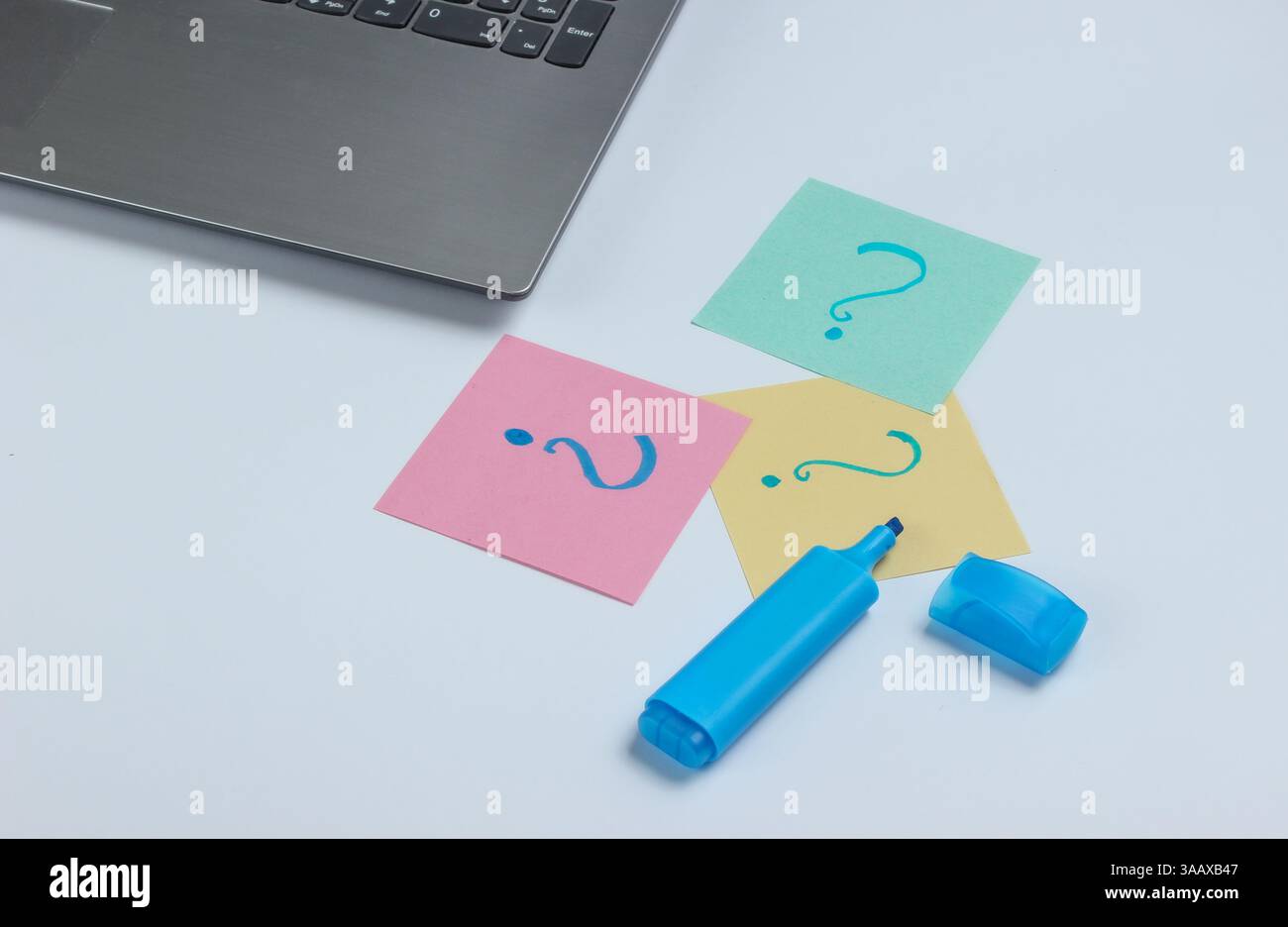 Laptop, fogli di carta con punti interrogativi disegnati e pennarello su sfondo bianco. Vista dall'alto Foto Stock