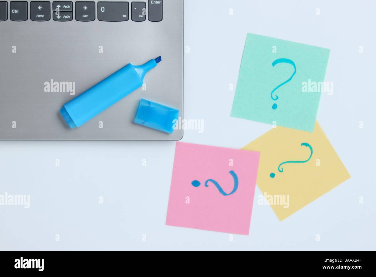 Laptop, fogli di carta con punti interrogativi disegnati e pennarello su sfondo bianco. Vista dall'alto Foto Stock