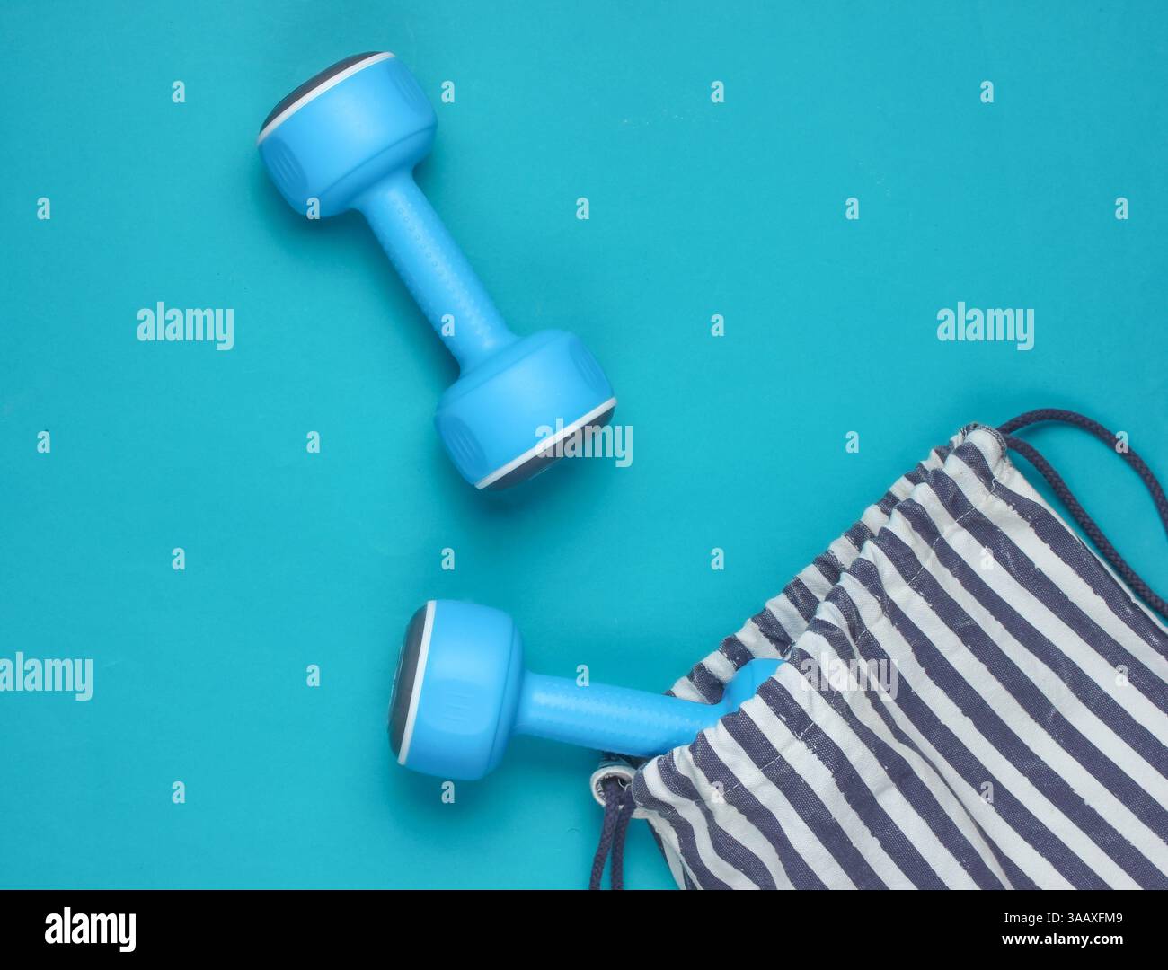 Borsa sportiva a righe con manubri su sfondo blu. Sport natura morta. Vista dall'alto. Foto Stock
