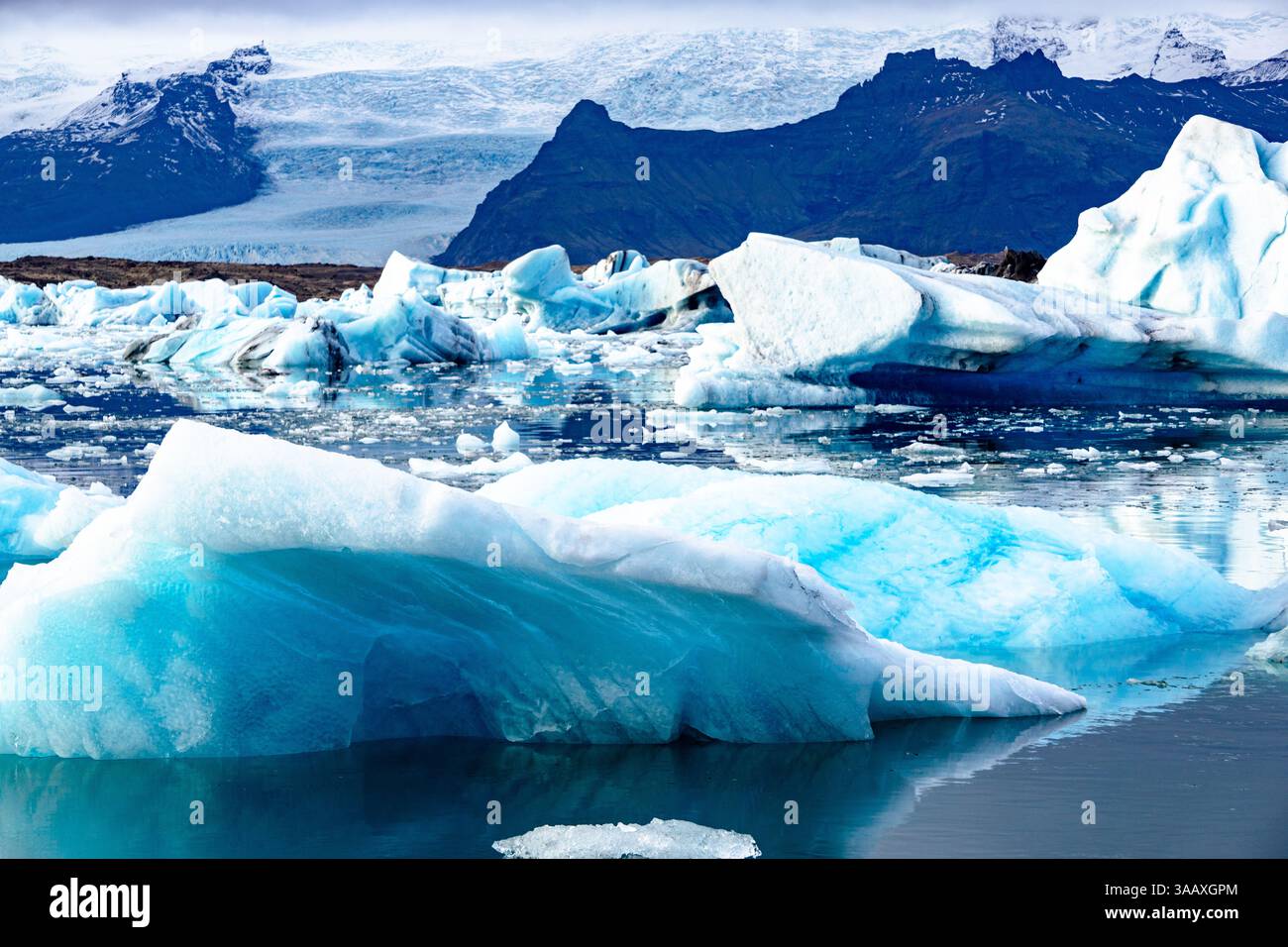 La Laguna del ghiacciaio di Jokulsarlon in Islanda presenta Iceberg blu brillante e serene acque artiche sotto un cielo limpido Foto Stock