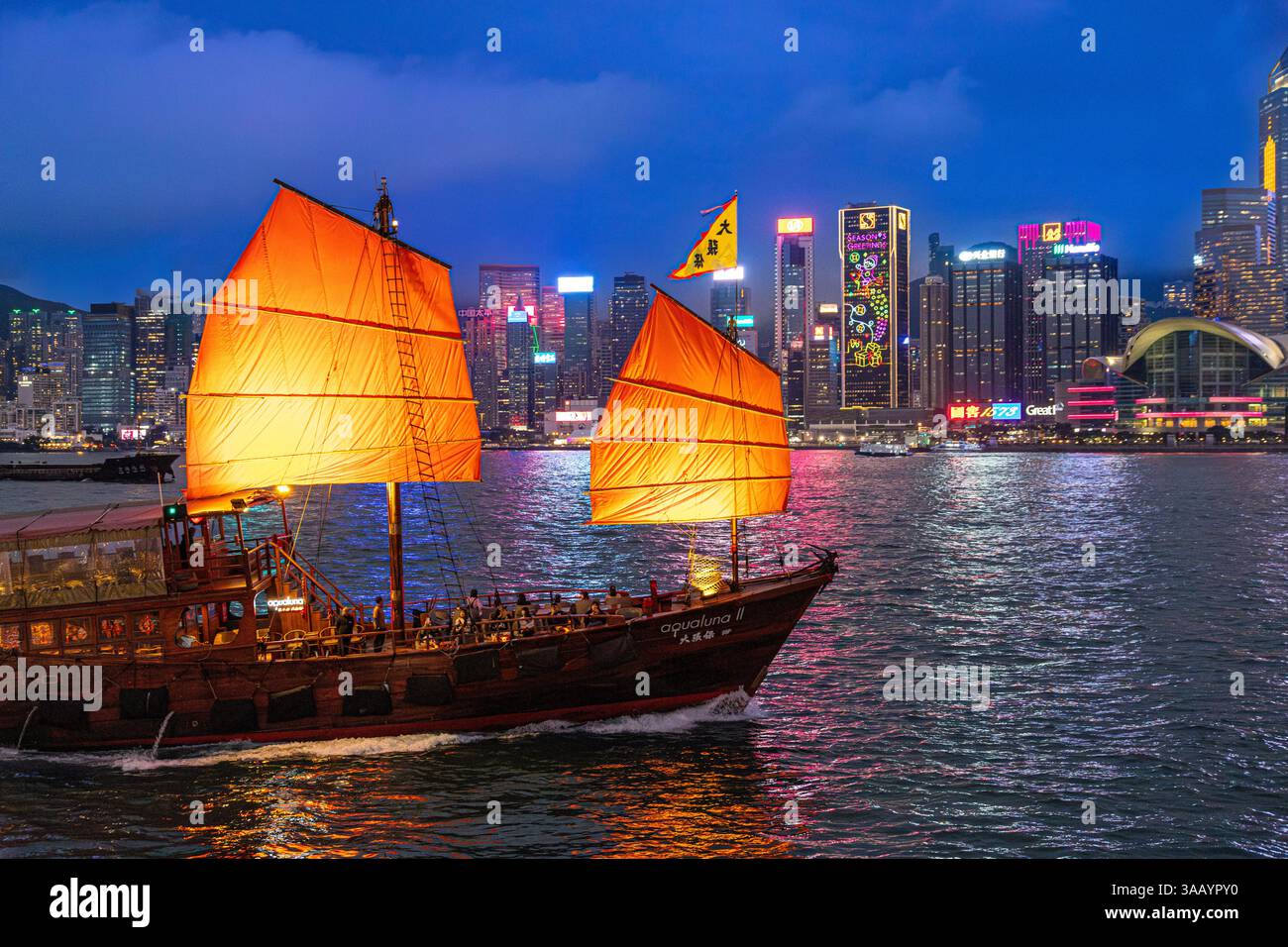 La barca a vela rossa Aqualuna II giunca in una crociera serale al crepuscolo nel Victoria Harbour, Kowloon, Hong Kong, Cina Foto Stock