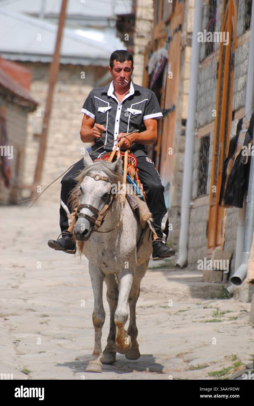 Lahic, Azerbaigian - Agosto 30, 2014. Cavaliere a cavallo sulla strada principale in Lahic villaggio di montagna di Azerbaigian. Foto Stock