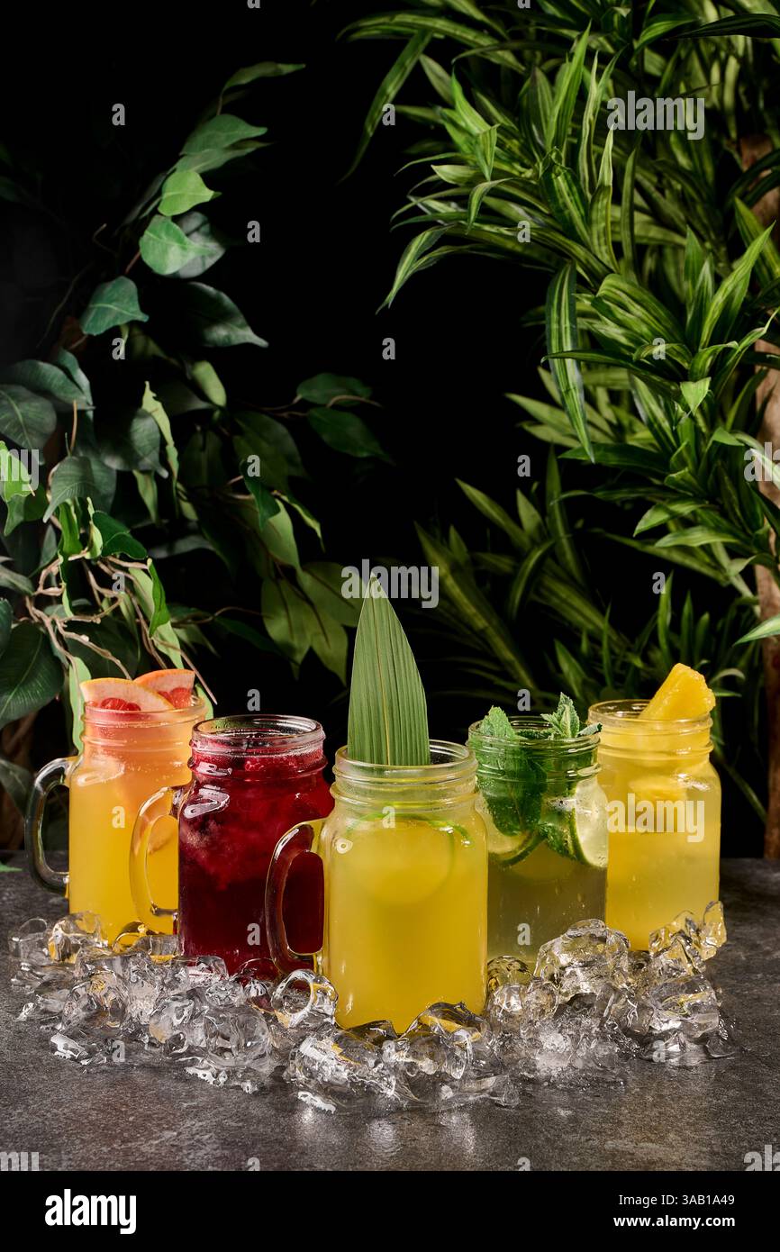 Varietà di limonata in vasetti mason con frutti di bosco e frutta. limonata estiva in un bicchiere con ghiaccio su sfondo scuro Foto Stock