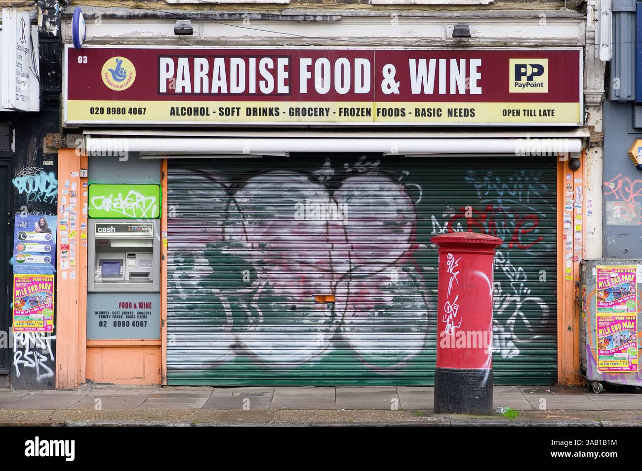 Cartolina rossa con graffiti e negozio chiuso coperto con persiane, ironicamente chiamato Paradise Food & Wine in Burdett Road, Mile End, Londra Foto Stock