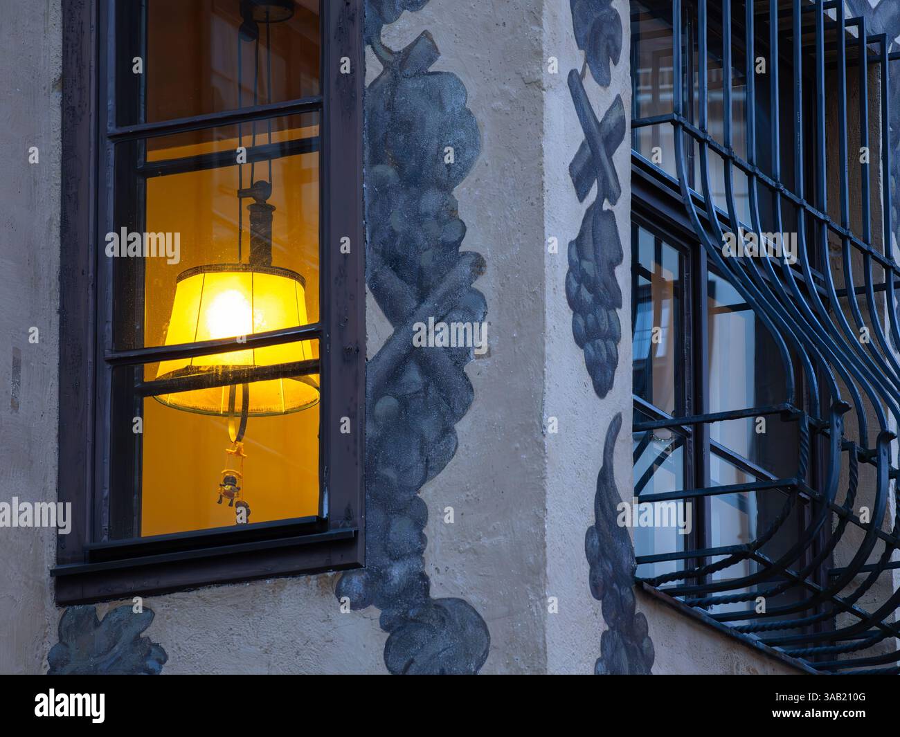 Una finestra illuminata con una lampada incandescente all'interno di una vecchia casa medievale a Innsbruck, circondata da pareti decorative e barre metalliche sulla finestra adiacente Foto Stock