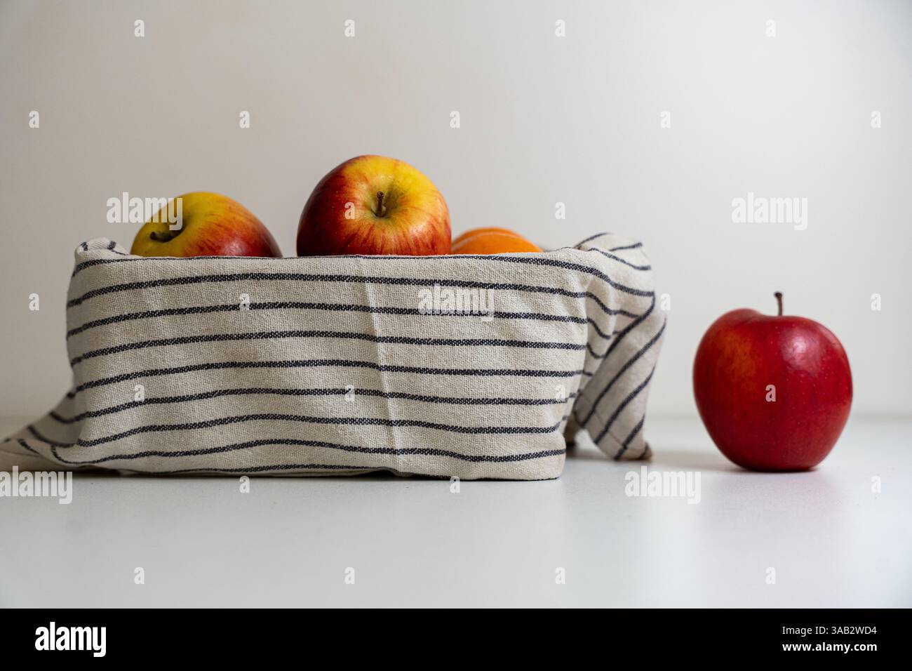 Un cestino di mele ricoperto da un telo con una mela accanto al cestello su sfondo bianco. Foto Stock