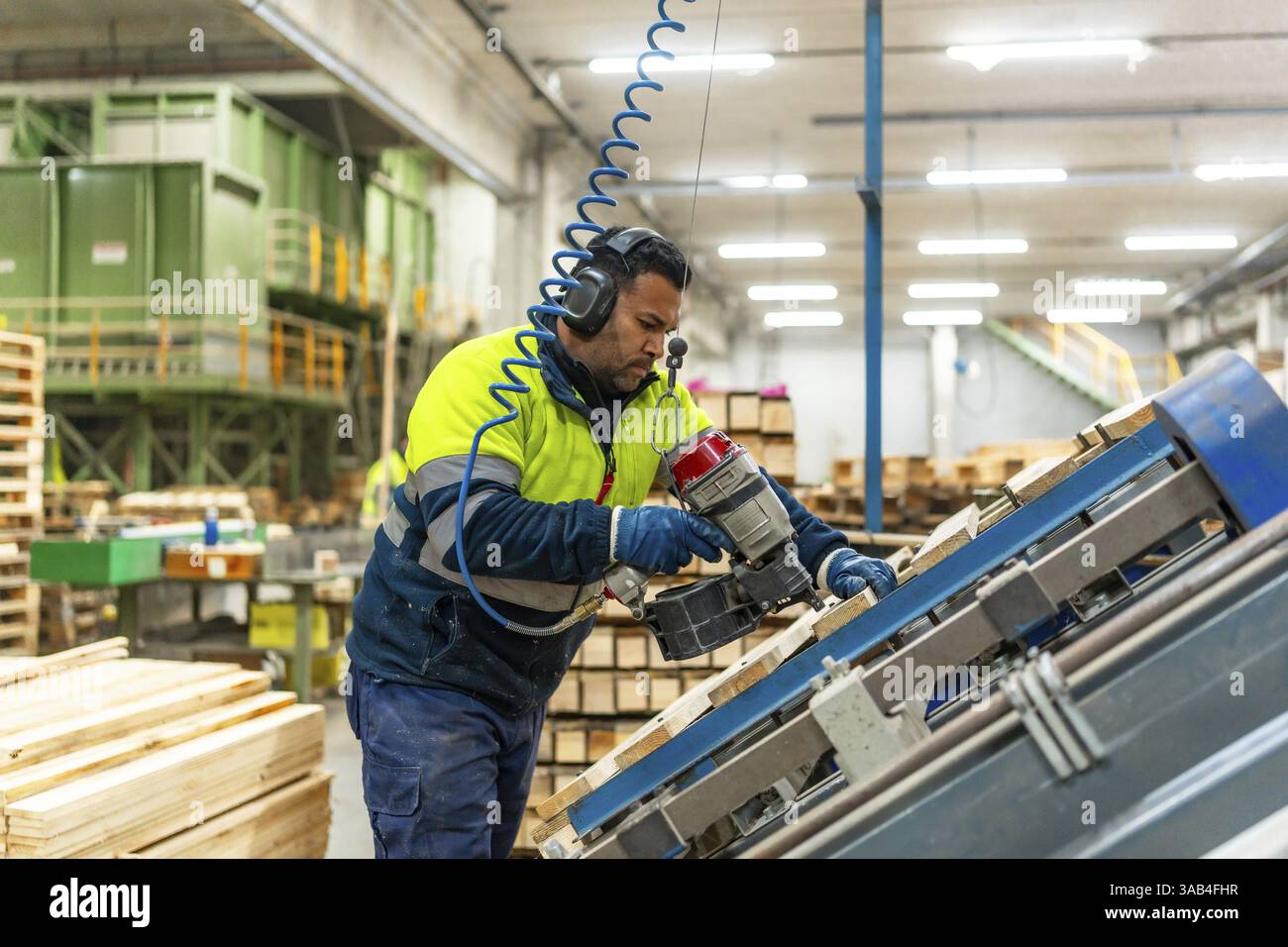 Vista laterale foto di tre quarti di lunghezza di un lavoratore caucasico che organizza pallet per riutilizzarli in uno stabilimento di riciclaggio Foto Stock