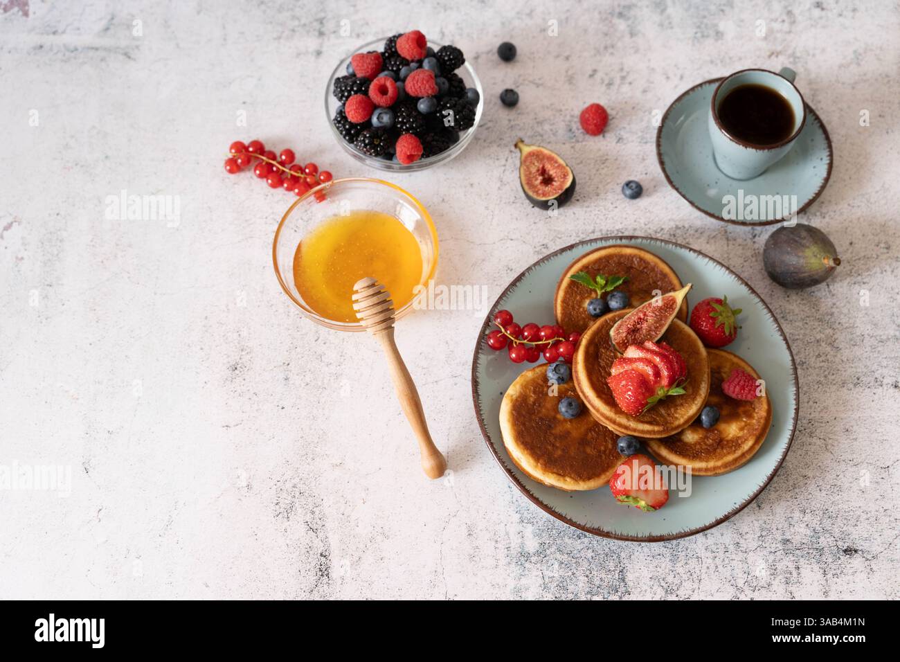Pancake fatti in casa con mirtilli, lamponi e fragole su un piatto bianco con un panno blu su un tavolo grigio chiaro Foto Stock