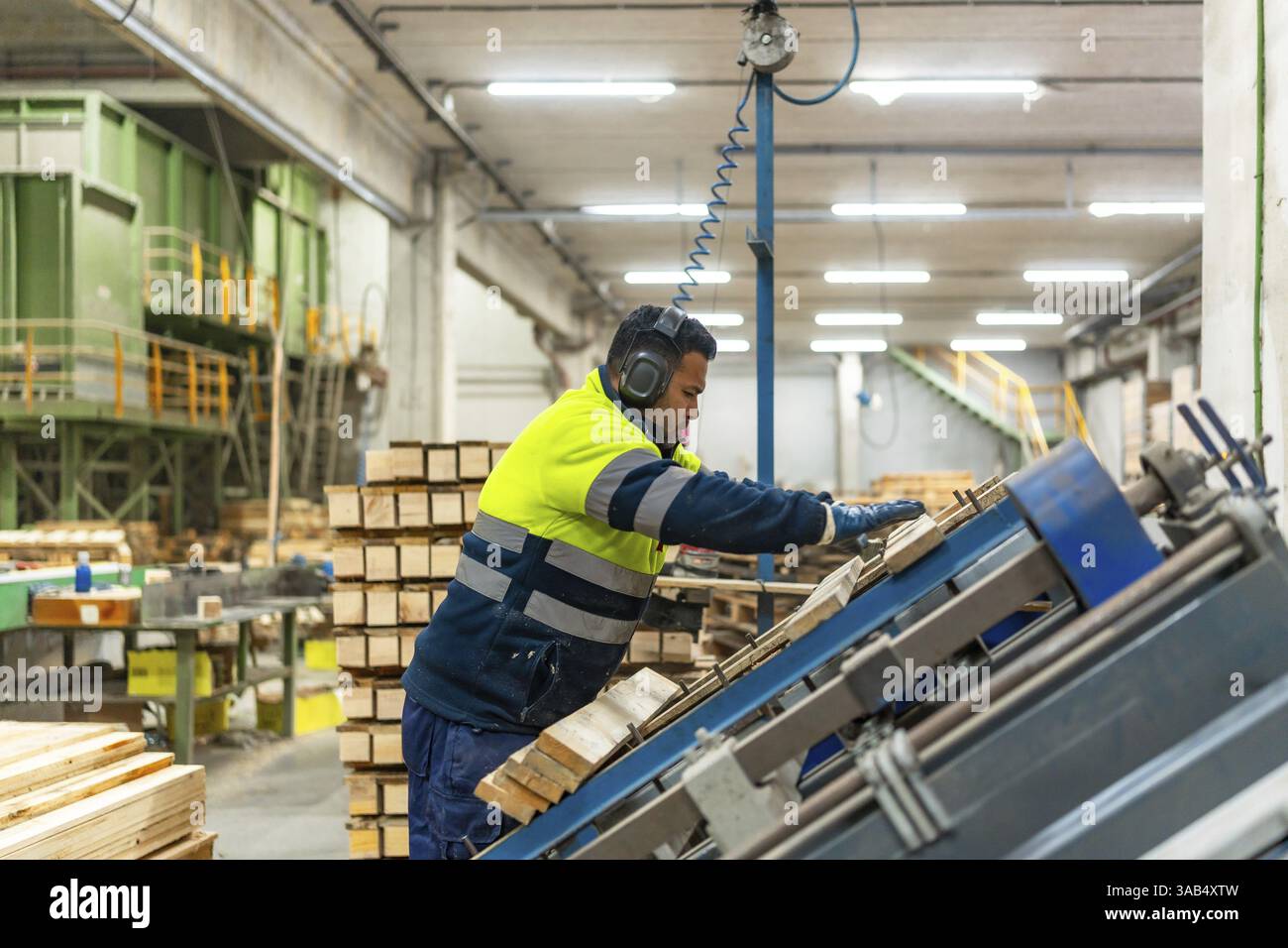 Vista laterale di un operatore con attrezzatura protettiva che ripara pallet nell'area di riciclaggio di un'officina Foto Stock