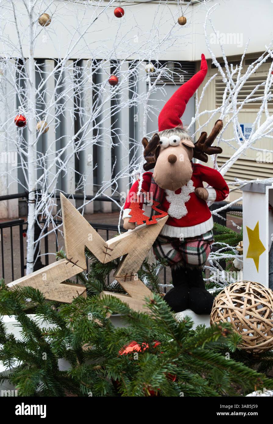 Colmar, Francia - 12 dicembre 2024: Una scena festosa con una lussuosa renna vestita da Babbo Natale, in piedi accanto a una stella di legno e circondata da Chri Foto Stock