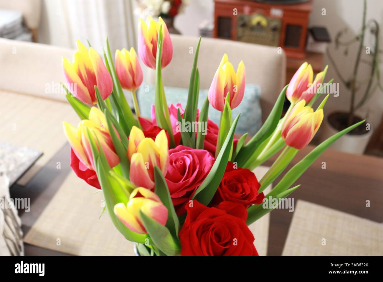 Bouquet colorato di tulipani e rose rosse in un accogliente ambiente interno Foto Stock