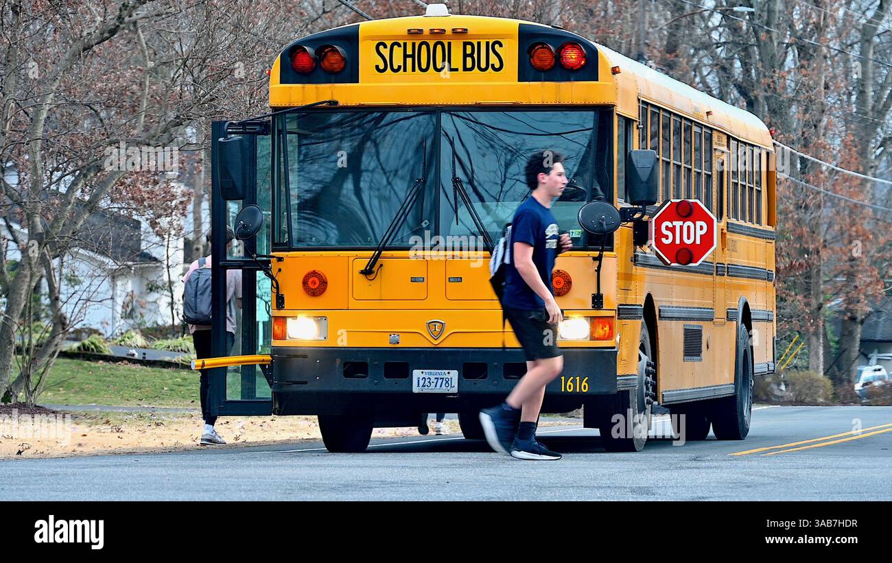Fairfax, Virginia, USA - 27 febbraio 2025: Uno studente delle scuole superiori attraversa la strada di fronte a uno scuolabus appena uscito nel suo quartiere. Foto Stock