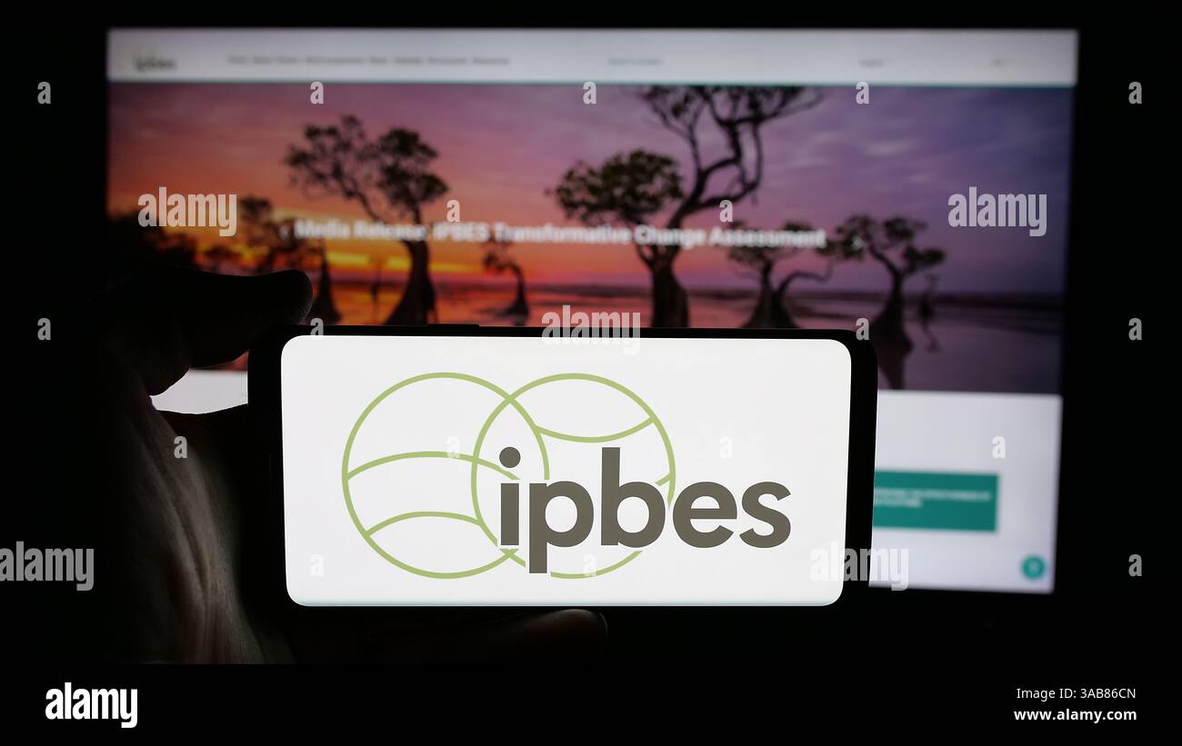 In questa immagine, una persona ha in mano un cellulare con il logo dell'organizzazione intergovernativa IPBES sullo schermo davanti alla pagina Web. Foto Stock