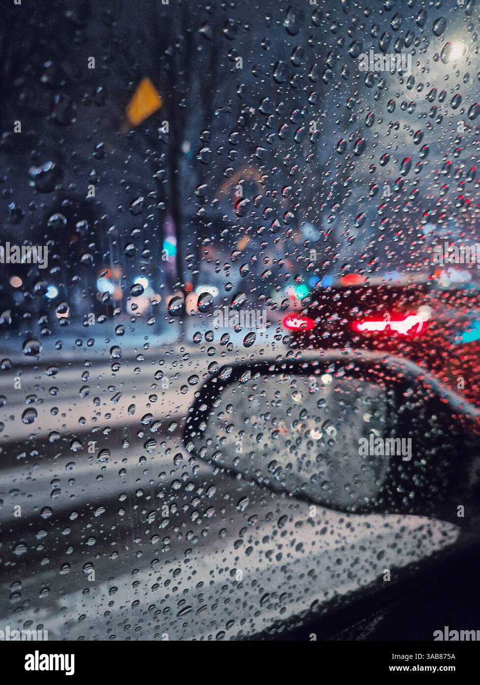 L'acqua di neve fusa gocciola sul finestrino della vettura con vista sullo specchietto retrovisore esterno. Traffico urbano notturno d'inverno - Immagine stock catturata con smartphone