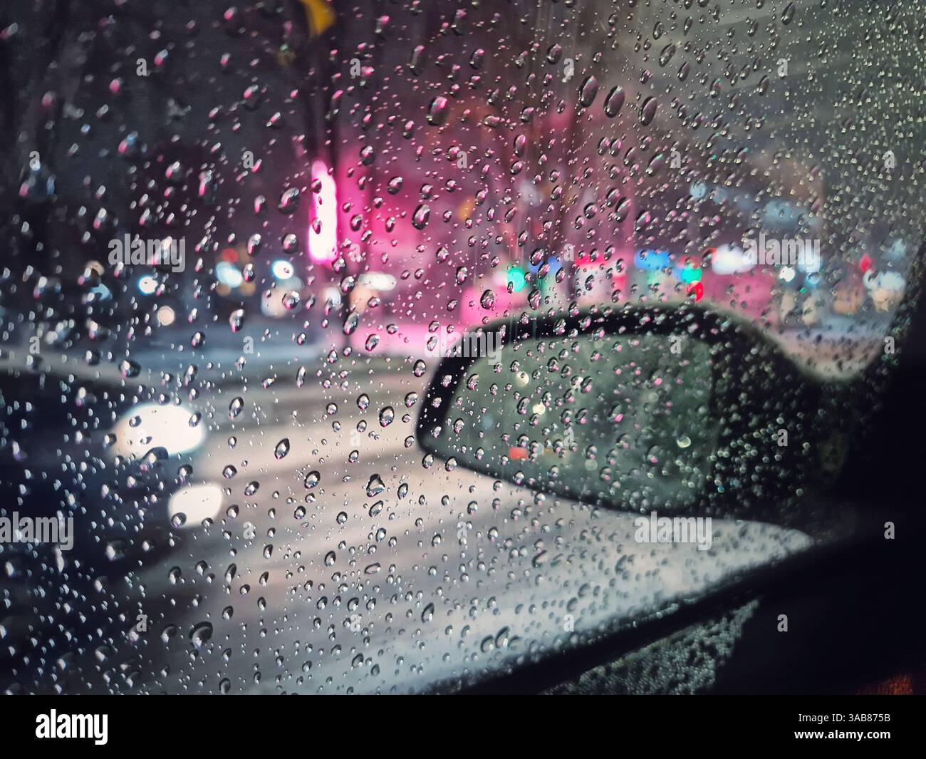 Lo scioglimento di acqua di neve gocciola sul finestrino della vettura con vista sullo specchietto retrovisore esterno. Scena urbana notturna d'inverno - Immagine stock catturata con smartphone
